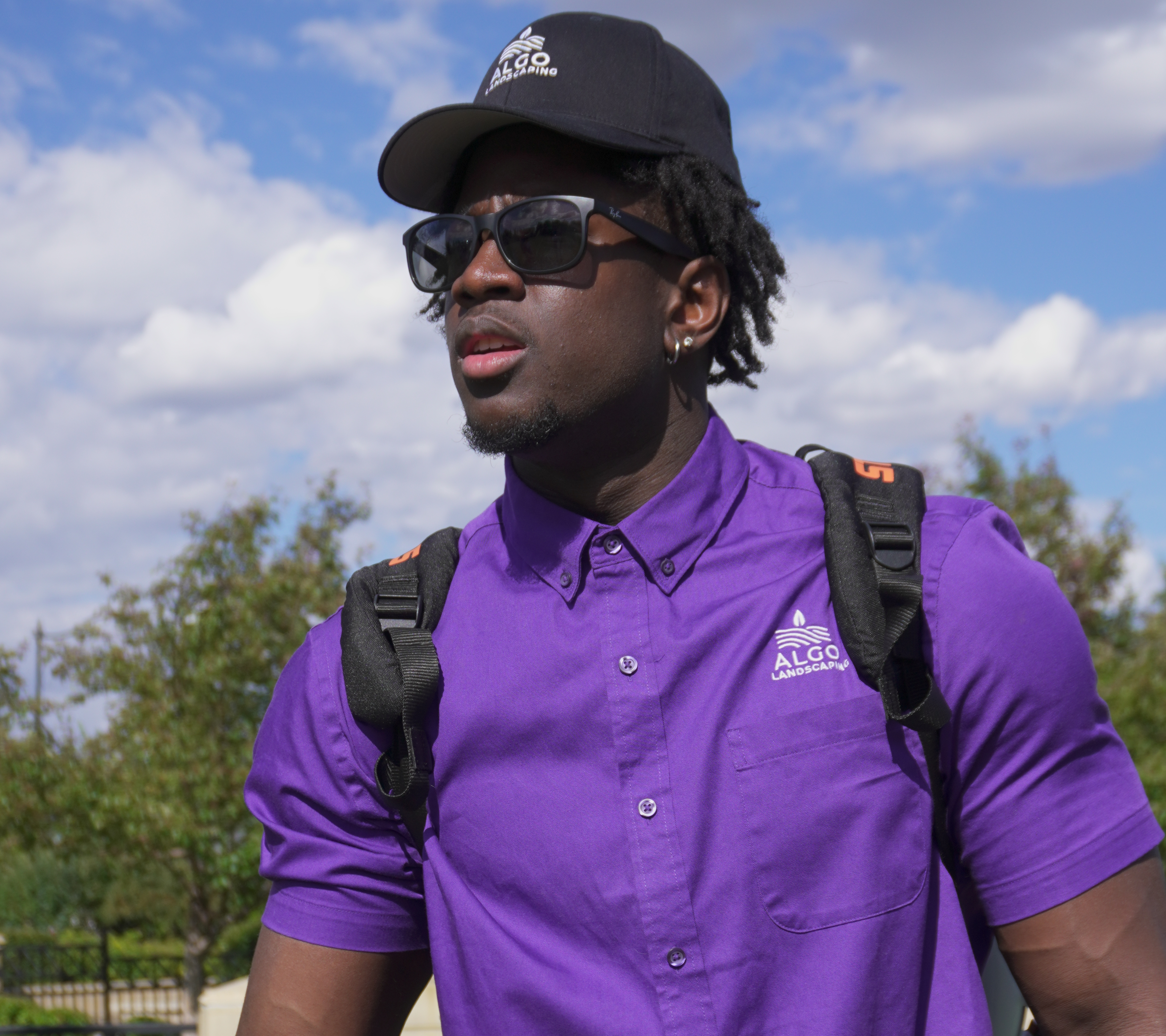 Algo Landscaping crew member wearing branded purple uniform and cap outdoors in Calgary.